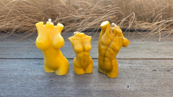Drei gelbe Kerzen in Form von menschlichen Oberkörpern, auf einem Holztisch platziert.