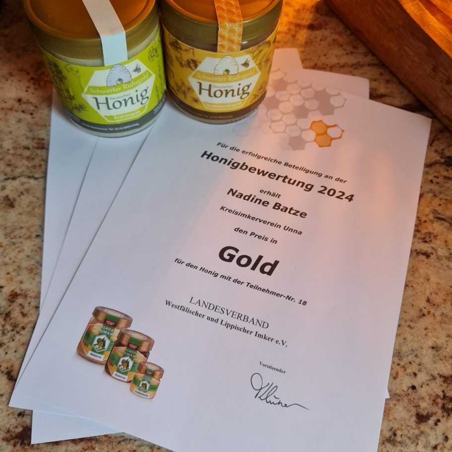 Zwei Honiggläser neben einem Zertifikat für die Goldauszeichnung 2024.